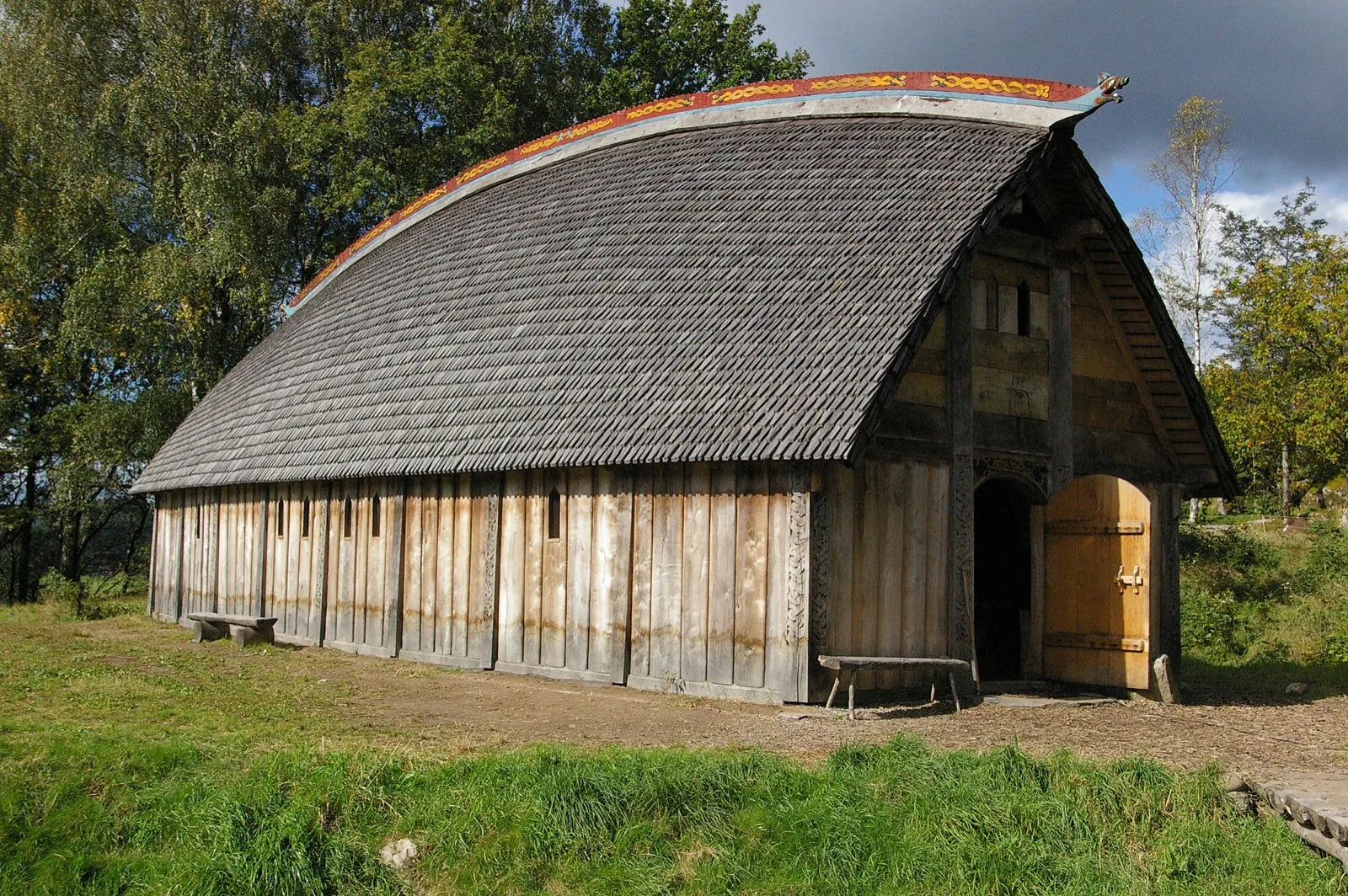The reconstructed longhouse at Ale Vikingagård with a curved shingle roof, painted gable ridge and an open arched door