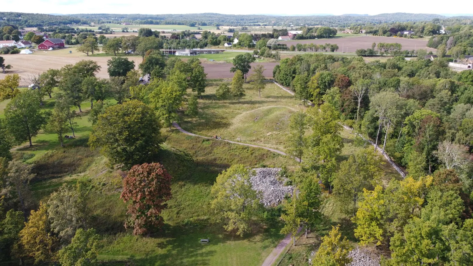 An aerial view over Borre Park with grass-covered Viking Age burial mounds among old oaks, footpaths crossing the parkland and farmland beyond