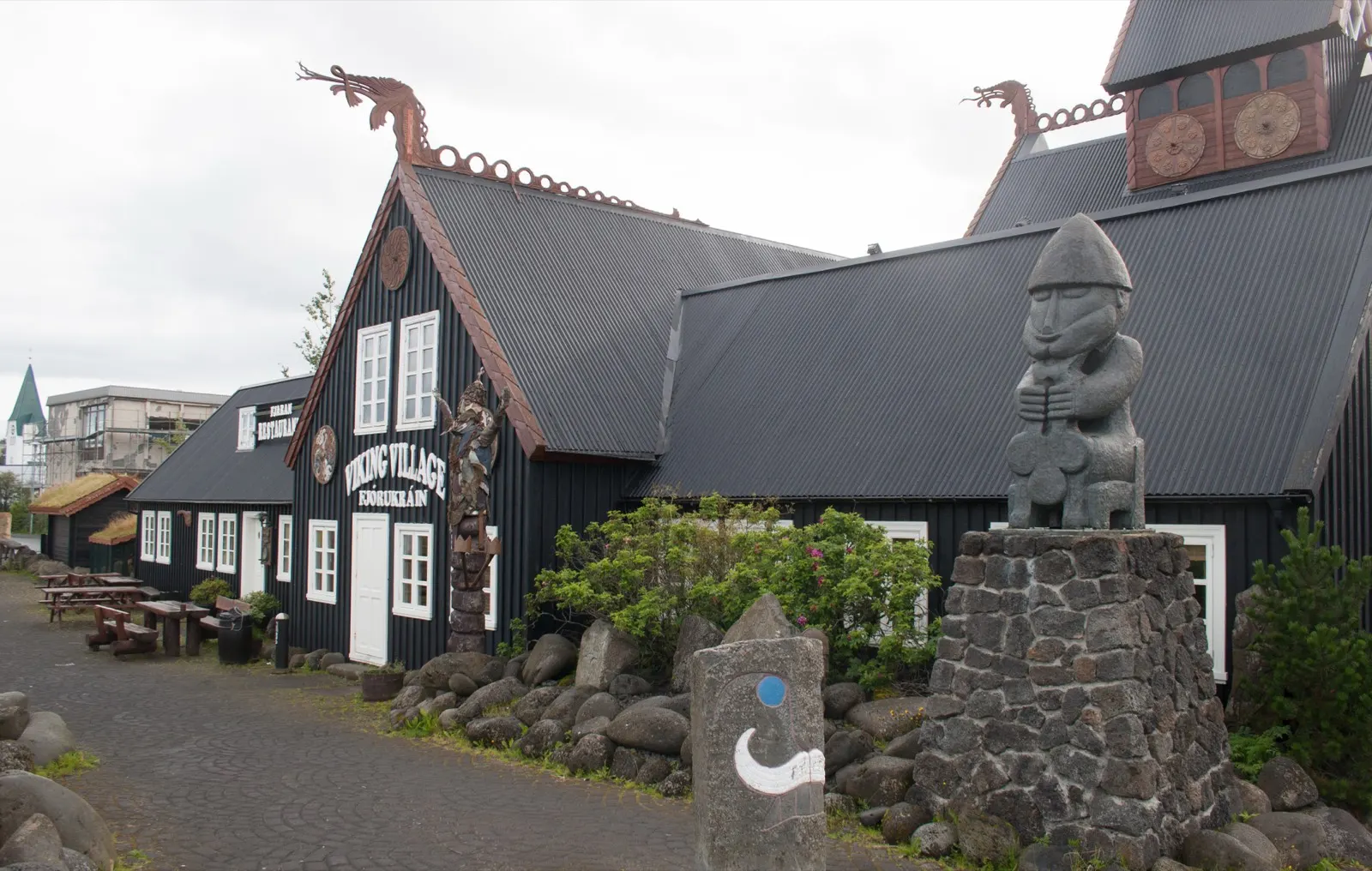 The black timber Viking Village building in Hafnarfjörður with dragon-head gables, a carved wooden figure on a stone plinth in front