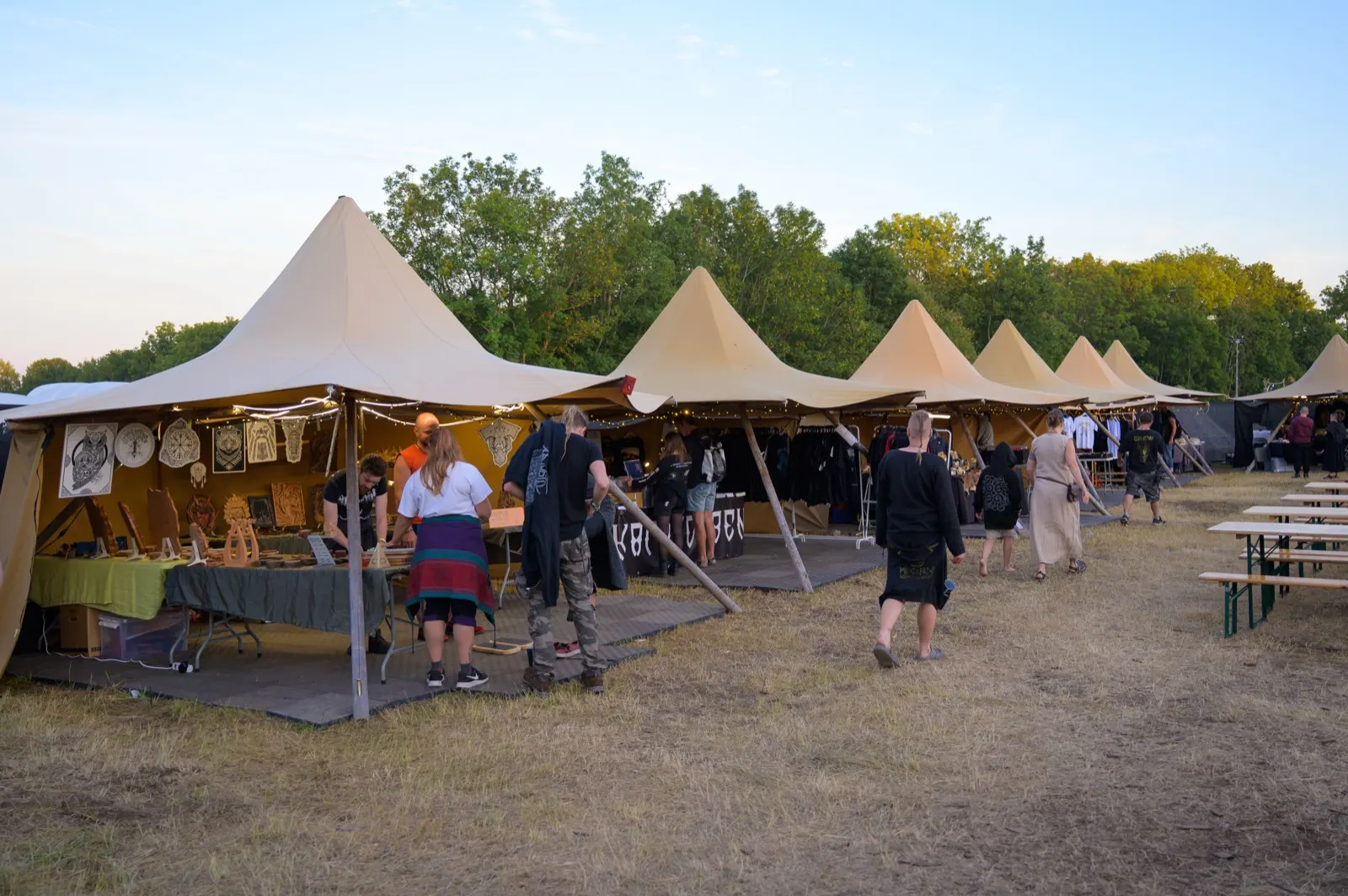 A row of pointed canvas market tents strung with lights in the Kaupangr market area at dusk, vendors and festivalgoers browsing