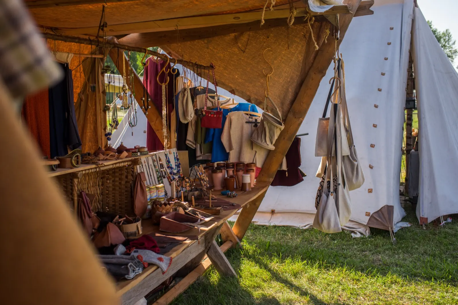 A market stall under a canvas tent at the Saltvik Viking market with leather bags, wooden tankards and hand-dyed tunics hanging from the frame