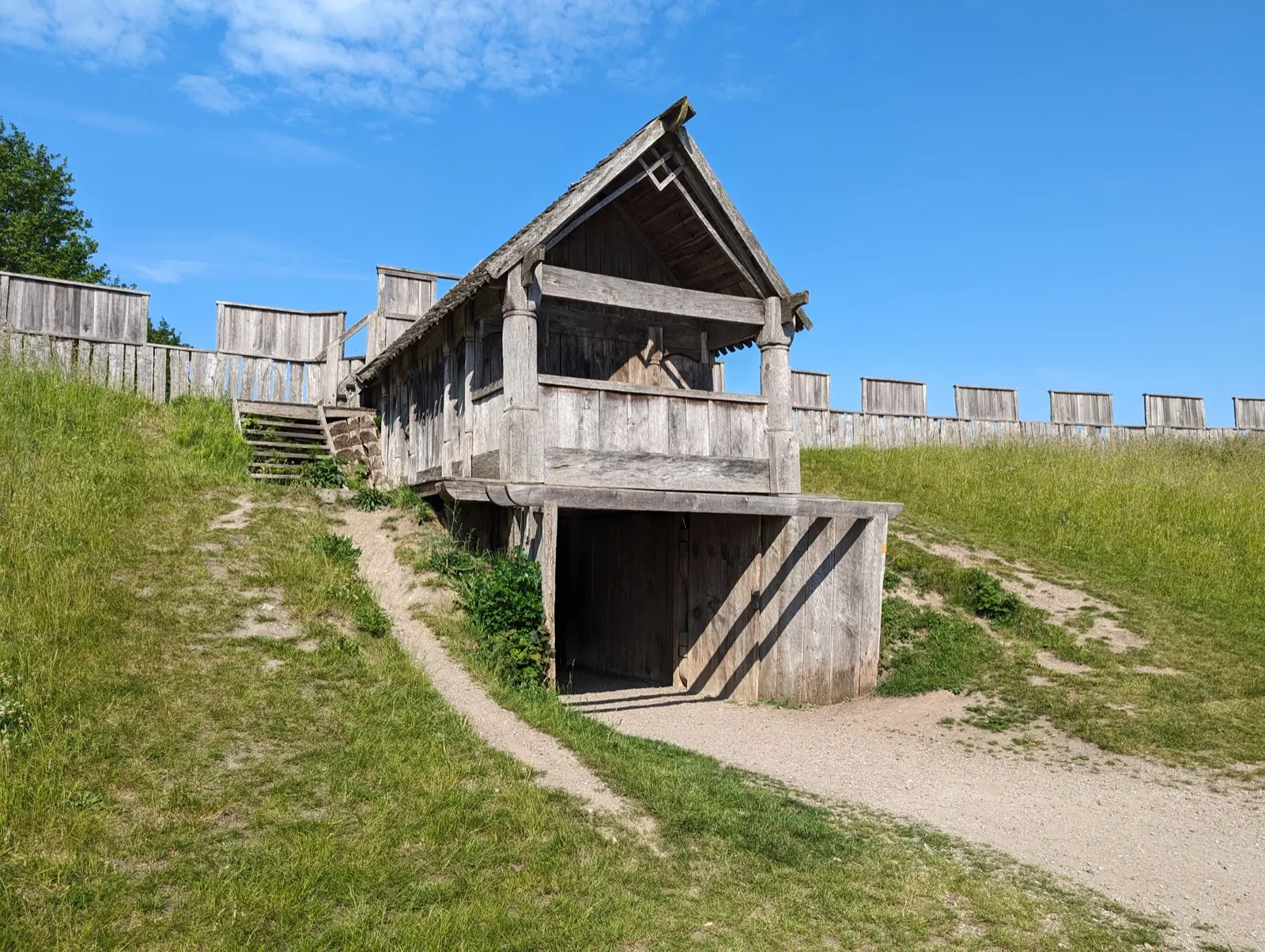 The reconstructed timber gate tower and palisade of Trelleborgen on a grass rampart under a blue sky